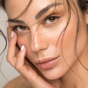 Close up studio shot of a beautiful brunette woman with glowing skin. Holding hands near her face.